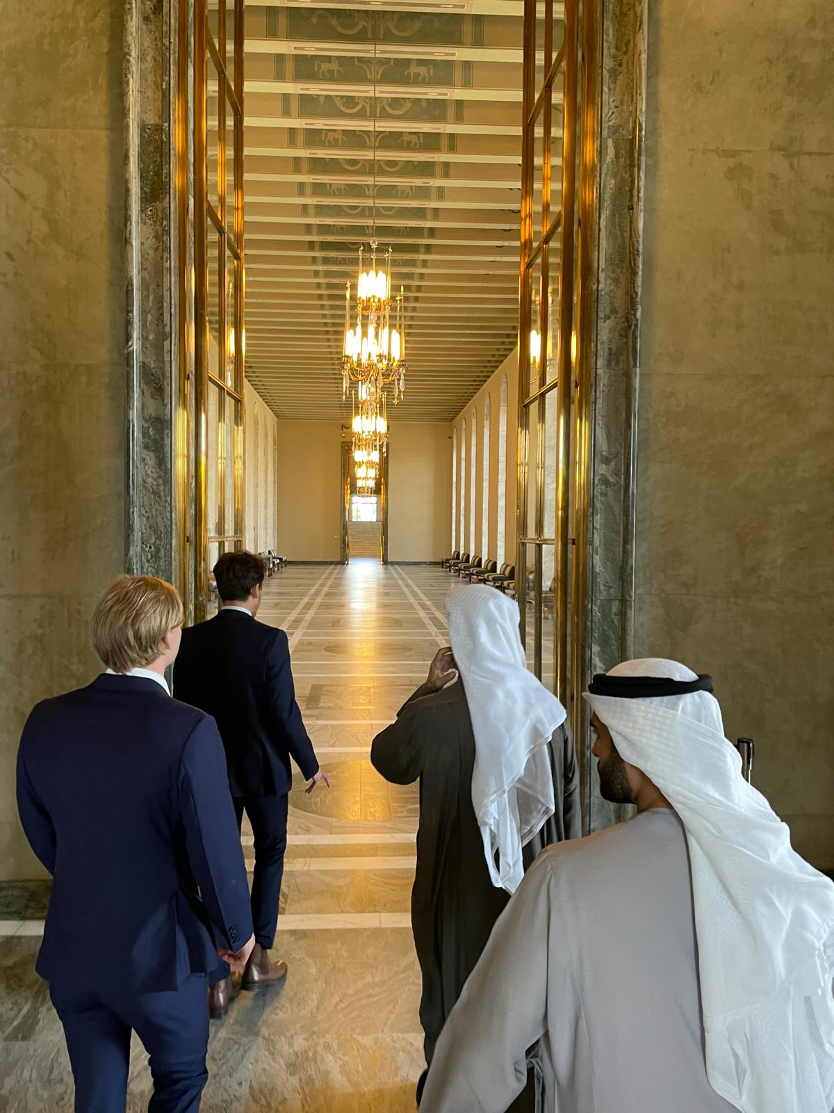 A delegation walking through a marble and brass state corridor